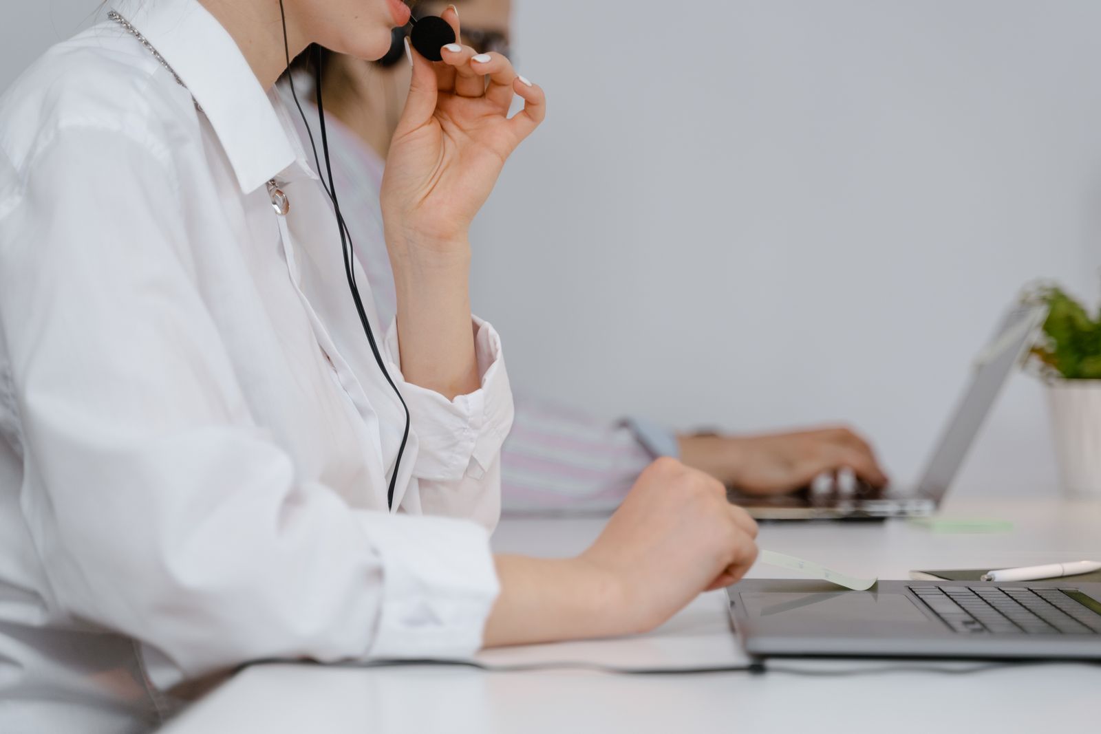 Eine Person justiert ein Headset-Mikrofon beim Diktieren am Laptop; ein einfaches Headset löst die Audioqualität in gemeinsamen Räumen